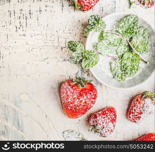 Fresh sliced Strawberries with powdered sugar and mint leaves in bowl on light rustic background, top view