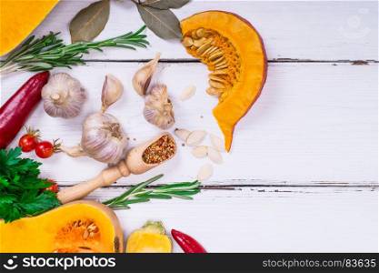 fresh slices of pumpkin and garlic with spices on a white wooden background, empty space on the right, top view