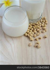 Fresh Soy milk (Soya milk) and dried soybean seeds on wooden background with white plumeria flower. Traditional staple of East Asian cuisine