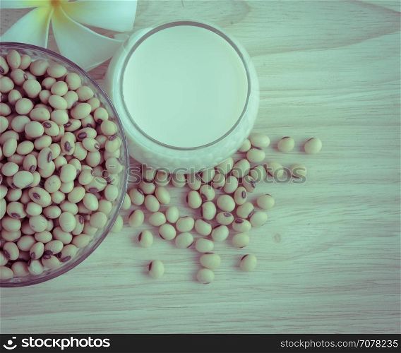 Fresh Soy milk (Soya milk) and dried soybean seeds on wooden background with white plumeria flower. Retro-Vintage filter effect
