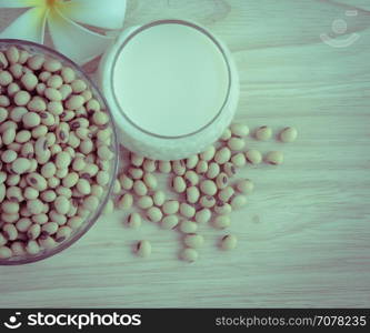 Fresh Soy milk (Soya milk) and dried soybean seeds on wooden background with white plumeria flower. Retro-Vintage filter effect