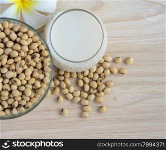 Fresh Soy milk (Soya milk) and dried soybean seeds on wooden background with white plumeria flower. Traditional staple of East Asian cuisine