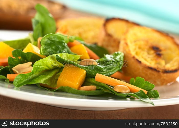 Fresh spinach, mango and carrot salad with peanuts on top and fried baguette slices in the back (Selective Focus, Focus on the mango piece in the front)