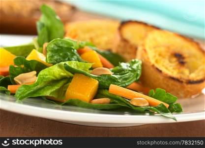 Fresh spinach, mango and carrot salad with peanuts on top and fried baguette slices in the back (Selective Focus, Focus on the mango piece in the front)