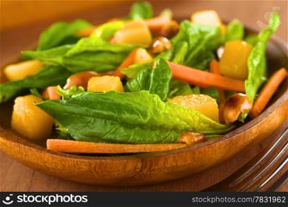 Fresh spinach, mango and carrot salad with peanuts on wooden plate with fork (Selective Focus, Focus on the spinach leaf in the front)