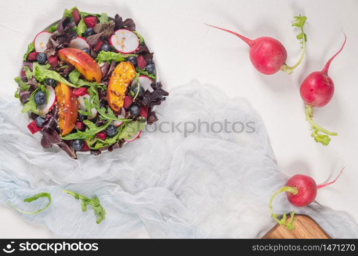 Fresh spring salad with rucola, lettuce, blueberries, radish, beet and slices of peach. White background with free text space