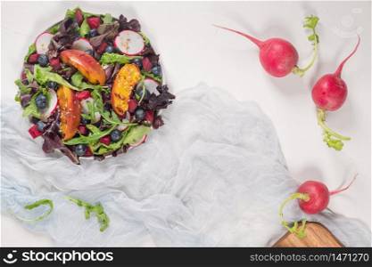 Fresh spring salad with rucola, lettuce, blueberries, radish, beet and slices of peach. White background with free text space