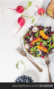 Fresh spring salad with rucola, lettuce, blueberries, radish, beet and slices of peach. White background with free text space. Top view