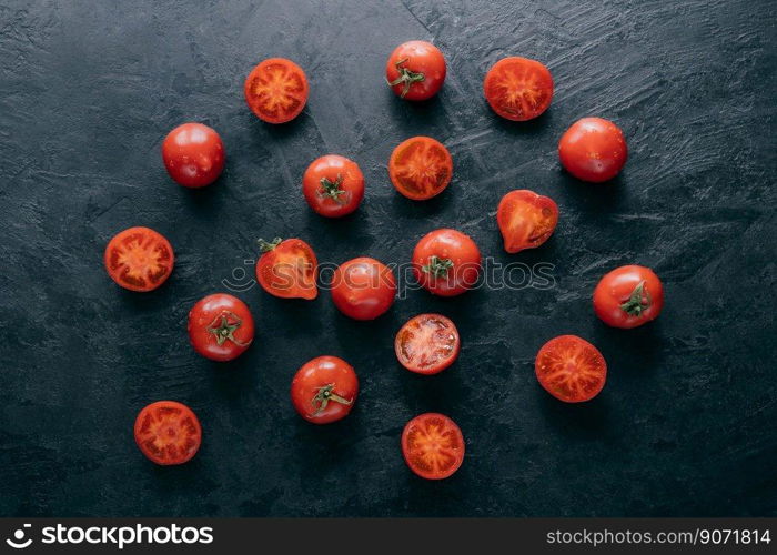 Fresh spring vegetables on dark background. Cherry ripe red tomatoes with green leaves, half sliced tomato, water drops. Organic food