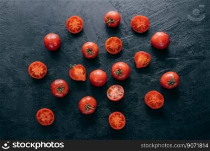 Fresh spring vegetables on dark background. Cherry ripe red tomatoes with green leaves, half sliced tomato, water drops. Organic food