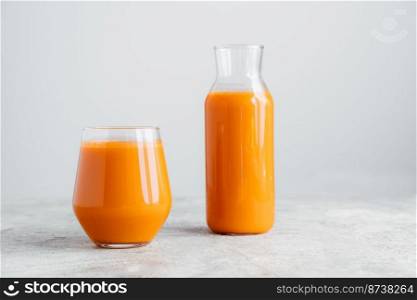 Fresh squeezed carrot juice in bottle and glass on wooden table isolated over white background. Vegetable beverage. Healthy drink.