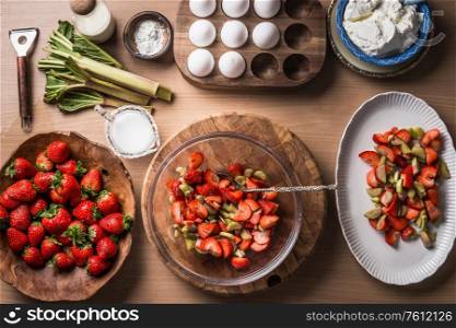 Fresh strawberries and rhubarb on wooden table background with ingredients for tasty seasonal cooking or baking. Top view. Healthy clean food. Paleo dieting. Home cuisine. Garden fruits eating