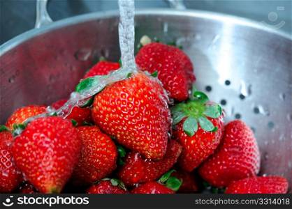 Fresh Strawberries. Fresh clear water splashing off ripe red strawberries in a stainless steel colander with water drops caught suspended in the air.