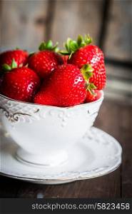 Fresh strawberries in a cup on wooden background