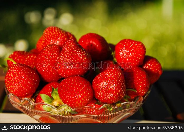 Fresh strawberries in a glass bowl on a table with green background