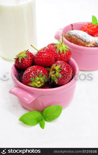 Fresh strawberries in a pink bowl, muffin and milk in the background