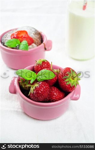 Fresh strawberries in a pink bowl, muffin and milk in the background