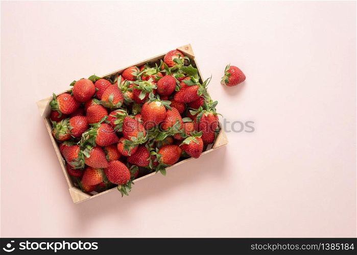 Fresh strawberries in a wooden box on a pink table above view. Homegrown strawberries harvested in a box. Organic fruits.