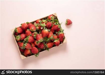 Fresh strawberries in a wooden box on a pink table above view. Homegrown strawberries harvested in a box. Organic fruits.