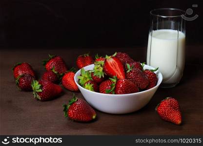 Fresh strawberries in ceramic bowl and a glass of milk on dark wooden background. Selective focus. - Image