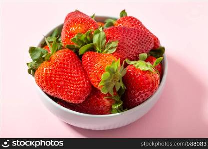 Fresh strawberries in ceramic bowl on pink background