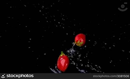 Fresh strawberries splashing on water on black background. Healthy eating concept. Fresh fruits background. Slow motion footage.