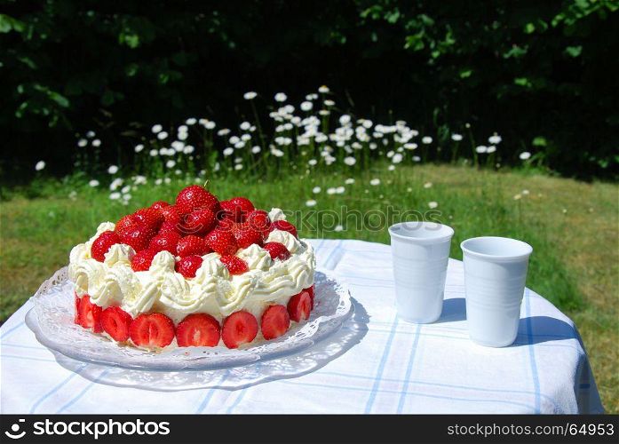 Fresh strawberry cake and two mugs on a table in a garden with blossom daisies