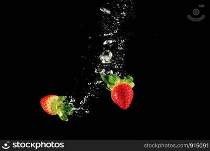 Fresh strawberry dropped into water with splash on isolated black background.