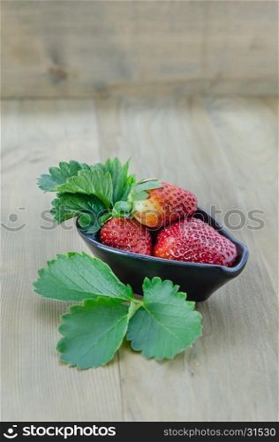 fresh strawberry fruits . fresh strawberry fruits in black bowl with green leaves over wooden background