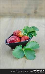 fresh strawberry fruits . fresh strawberry fruits in black bowl with green leaves over wooden background
