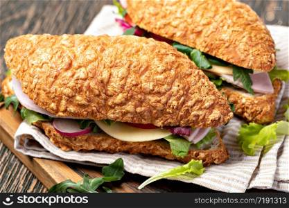 fresh submarine sandwich with ham, cheese, bacon, tomatoes, lettuce, on wooden cutting board. fresh submarine sandwich