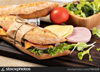 fresh submarine sandwich with ham, cheese, bacon, tomatoes, lettuce, on wooden cutting board. fresh submarine sandwich