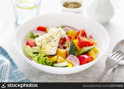 Fresh summer vegetable salad with lettuce, tomato, cucumber, bell pepper, onion and feta cheese, dressed with olive oil