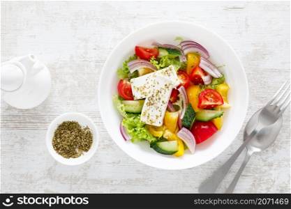 Fresh summer vegetable salad with lettuce, tomato, cucumber, bell pepper, onion and feta cheese, dressed with olive oil. Top view