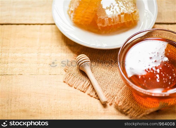 Fresh sweet honey in jar with wooden dipper and honeycomb on white plate on wood table background