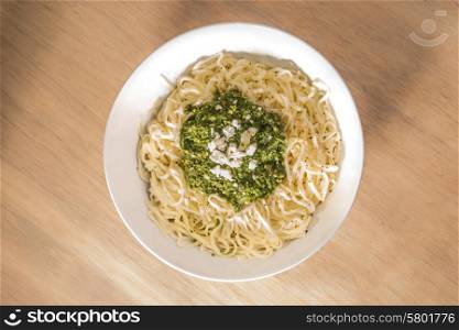 Fresh Tagliatelle pasta topped with basil pesto sauce in a bowl on a wooden surface, viewed from above.