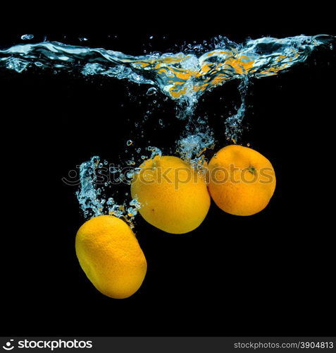 Fresh tangerines dropped into water with bubbles on black