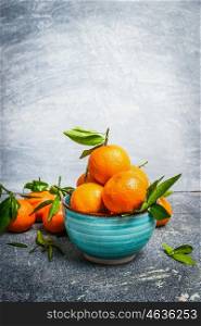 Fresh Tangerines with green leaves in blue bowl over rustic background, side view