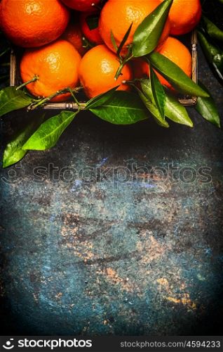 Fresh tangerines with green leaves on dark rustic background, top view, border