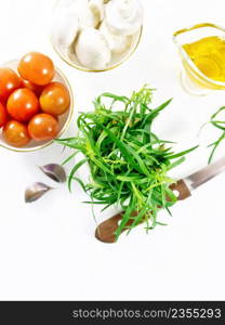 Fresh tarragon in a mortar, tomatoes and champignons in bowls, vegetable oil in gravy boat, garlic cloves and a knife on wooden board background from above