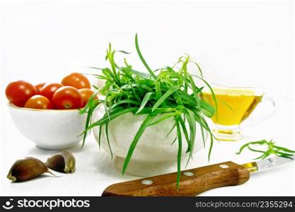 Fresh tarragon in a mortar, tomatoes and champignons in bowls, vegetable oil in gravy boat, garlic cloves and a knife on light wooden board background