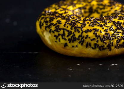 Fresh tasty colored donuts with sprinkles on black background