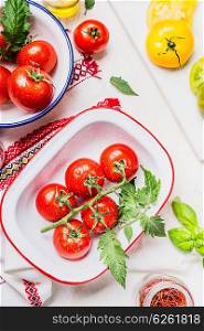 Fresh tasty colorful tomatoes in enamelled bowls on light kitchen table, ready for cooking or salad making, top view.