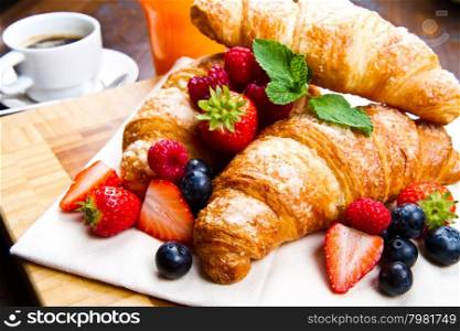 Fresh tasty croissants with berries on wooden background