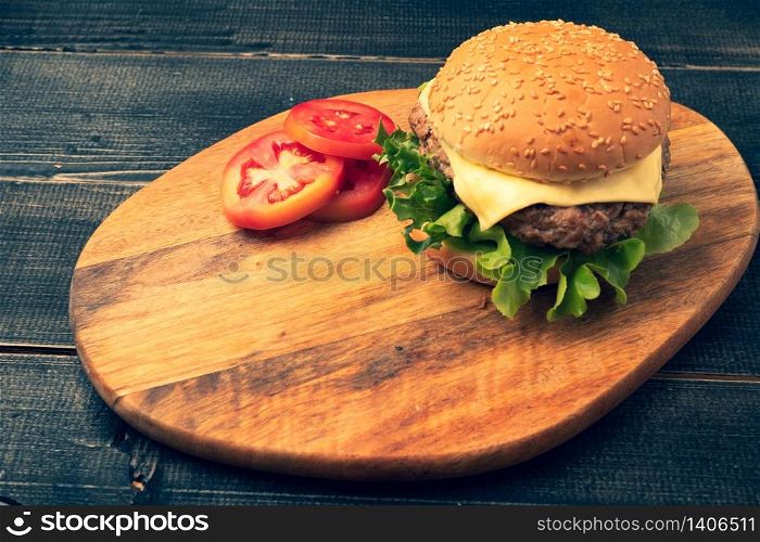 fresh tasty homemade hamburger with fresh vegetables, lettuce, tomato, cheese beside sliced tomatoes on a cutting board. Free space for text