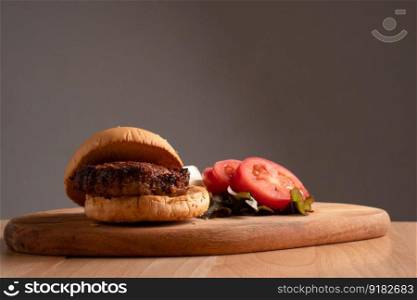 fresh tasty homemade hamburger with fresh vegetables, lettuce, tomato, cheese beside sliced tomatoes on a cutting board. Free space for text