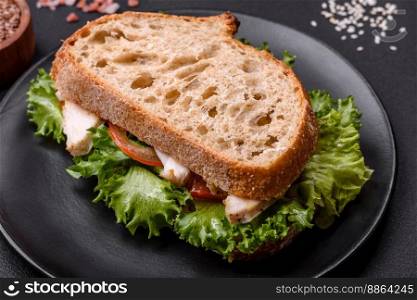 Fresh tasty sandwich with chicken, tomatoes and lettuce on a black plate on a dark concrete background