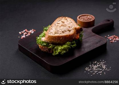 Fresh tasty sandwich with chicken, tomatoes and lettuce on a black plate on a dark concrete background