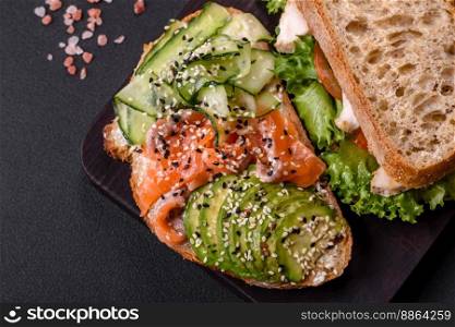 Fresh tasty sandwich with salmon, avocado and sesame and flax seeds on a dark concrete background
