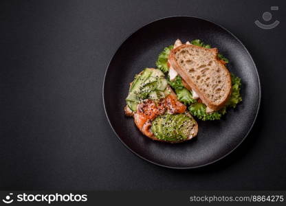 Fresh tasty sandwich with salmon, avocado and sesame and flax seeds on a dark concrete background